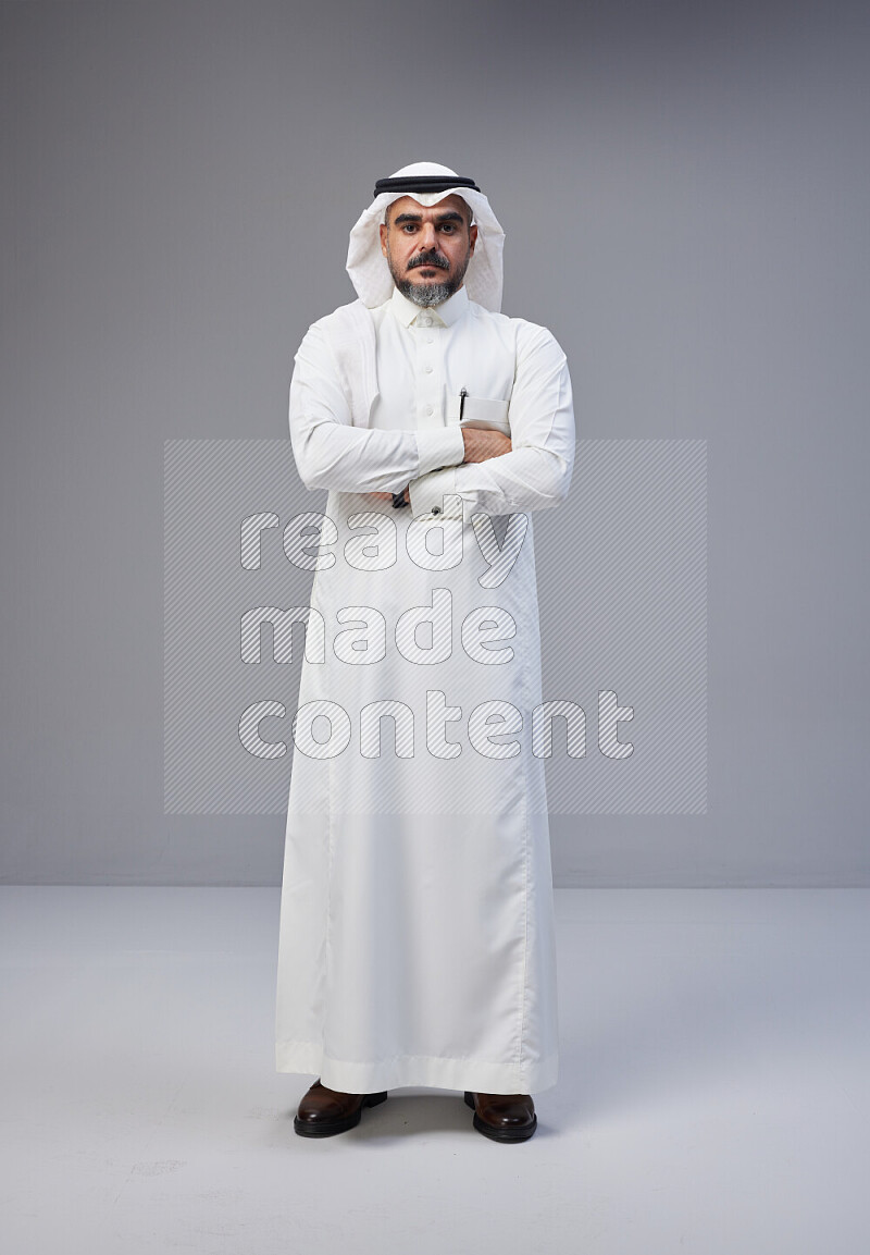 Saudi man Wearing Thob and white Shomag standing with crossed arms on Gray background