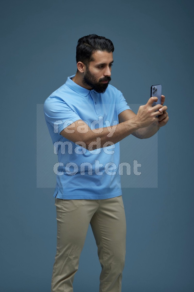 Man taking a picture with his phone  in a blue background wearing a Blue shirt