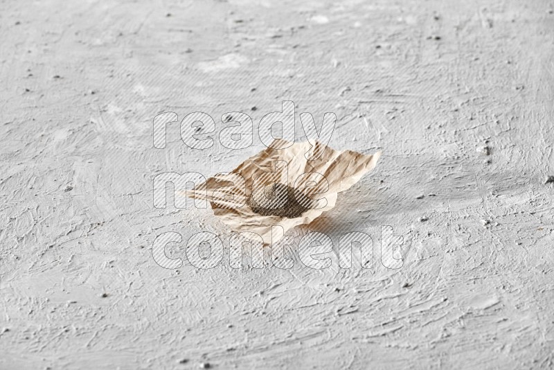 Black pepper powder on a crumpled paper on a textured white flooring