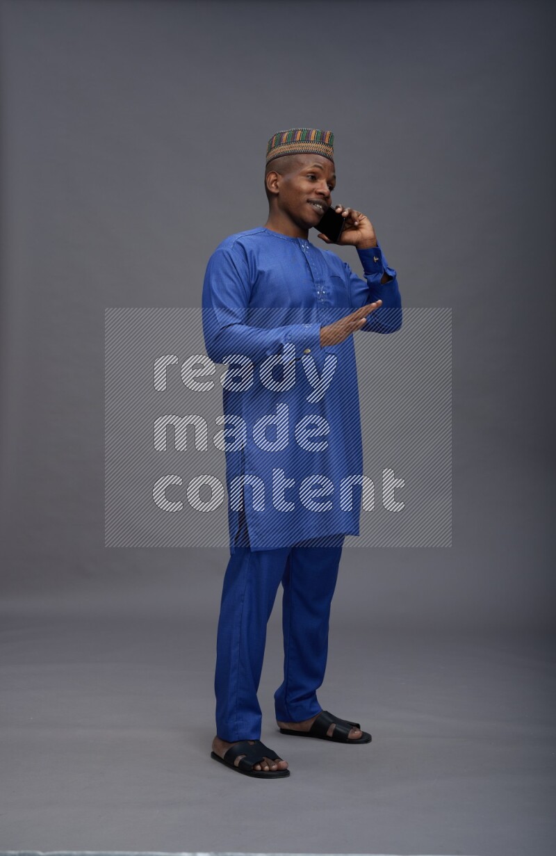 Man wearing Nigerian outfit standing talking on phone on gray background