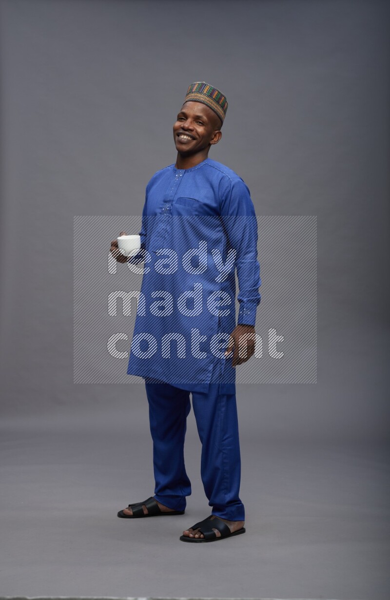 Man wearing Nigerian outfit standing holding mug on gray background