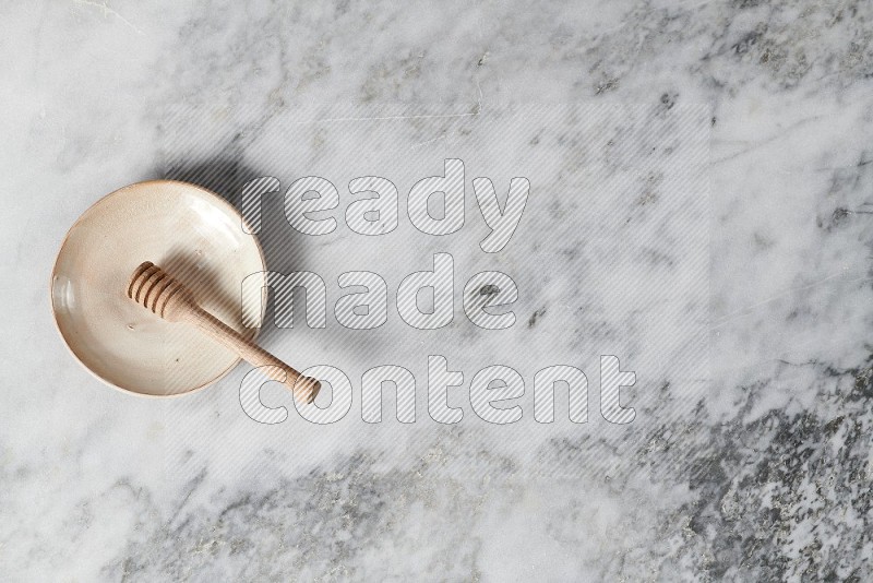 Beige Pottery Plate with wooden honey handle in it, on grey marble flooring, Top View