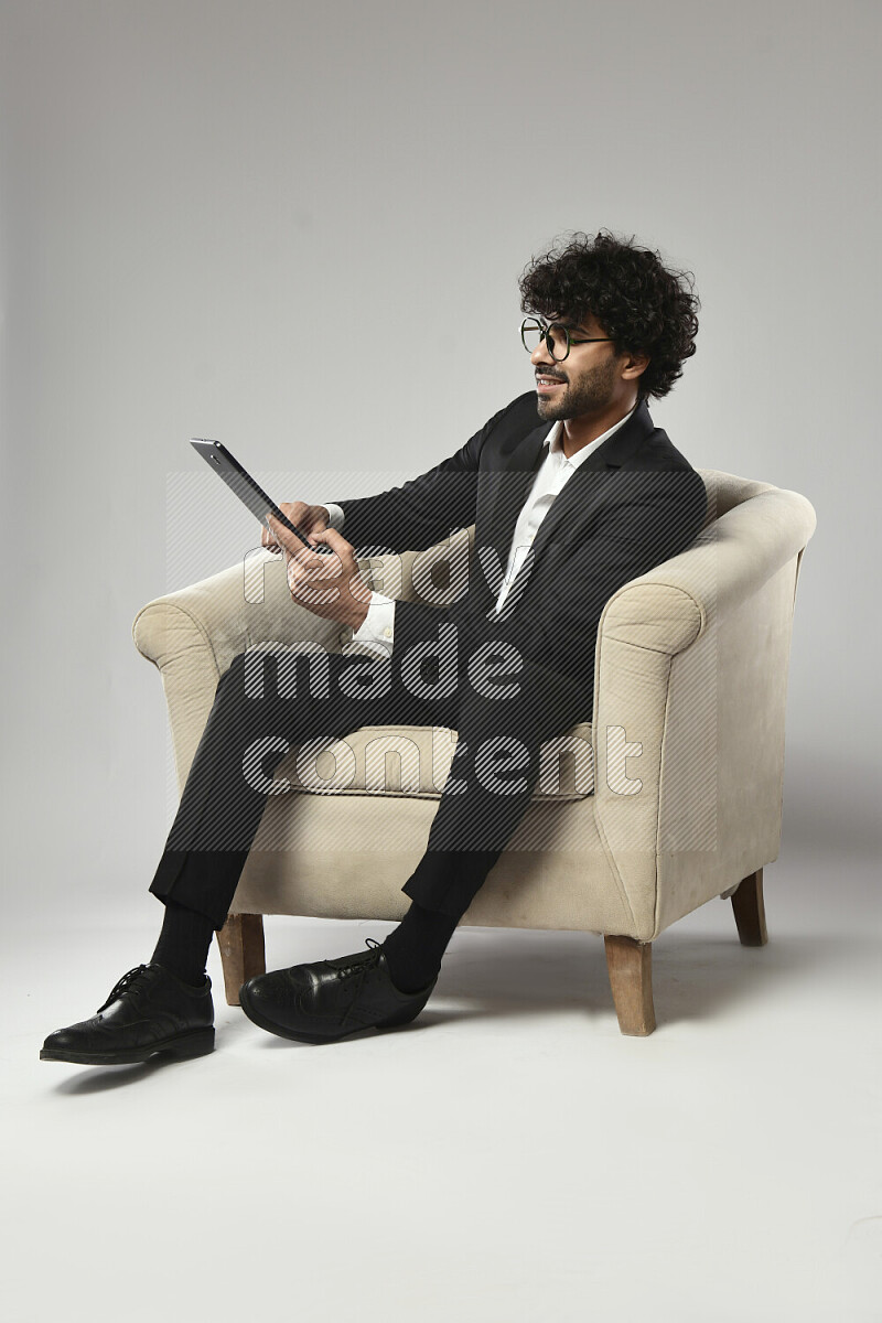 A man wearing formal sitting on a chair browsing on a tablet on white background