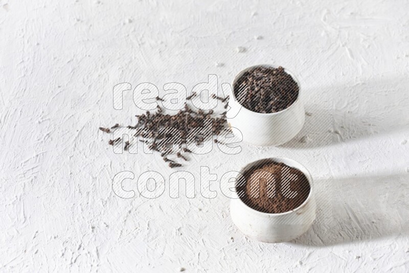 2 Beige ceramic bowls, one full of cloves and the other full of powder on textured white flooring