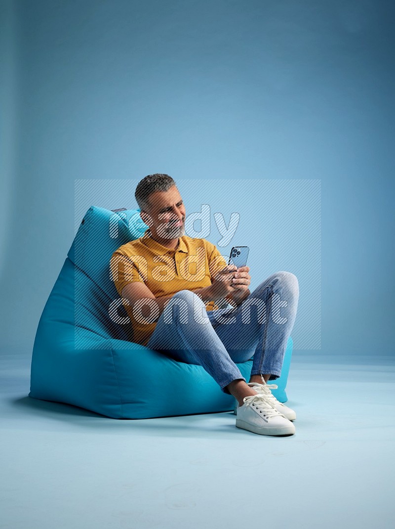 A man sitting on a blue beanbag and texting on phone