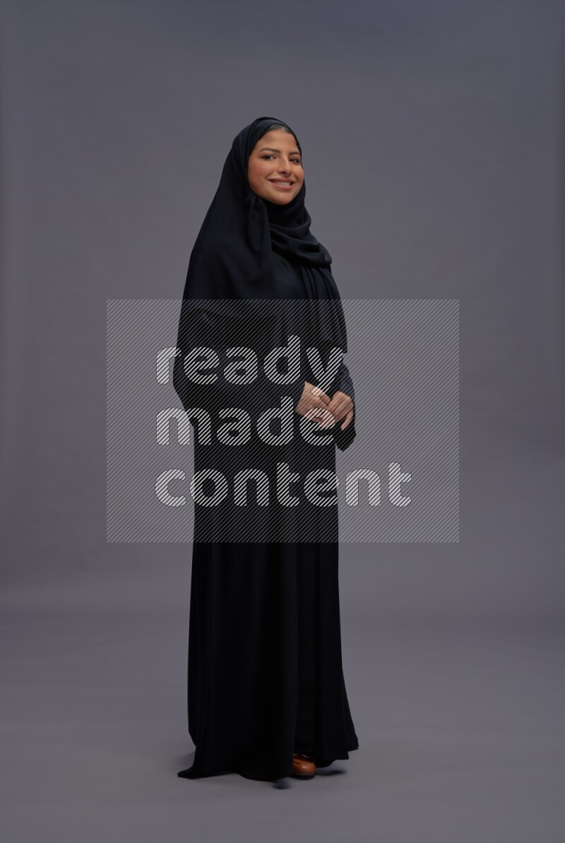 Saudi woman wearing Abaya standing interacting with the camera on gray background