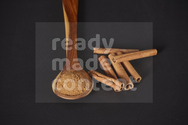 Cinnamon powder in a wooden ladle spoon beside it cinnamon sticks on the flooring on black background in different angles