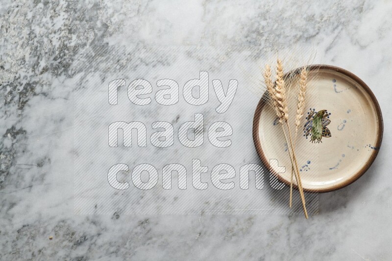 Wheat stalks on decorative pottery plate on grey marble background