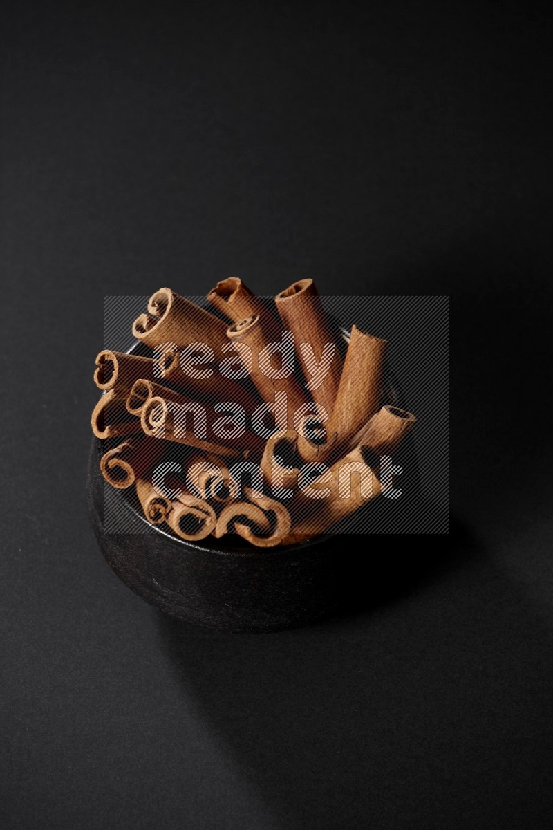 Cinnamon sticks in a black bowl on a black background in different angles