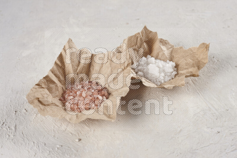 2 crumpled pieces of paper full of pink himalayan salt and white salt on white background
