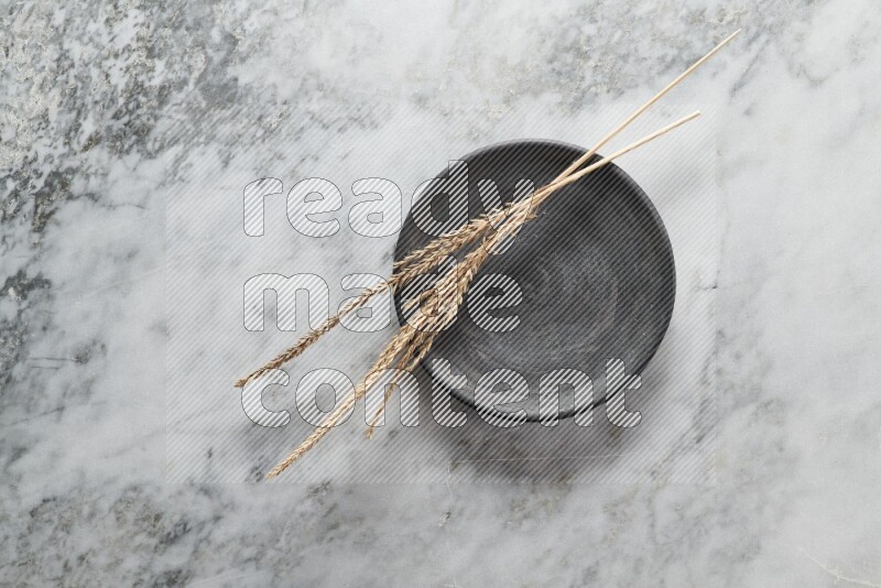 Wheat stalks on black pottery plate on grey marble background