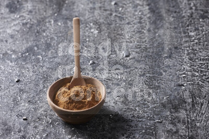Wooden bowl full of cinnamon powder with a wooden spoon on a textured black background in different angles