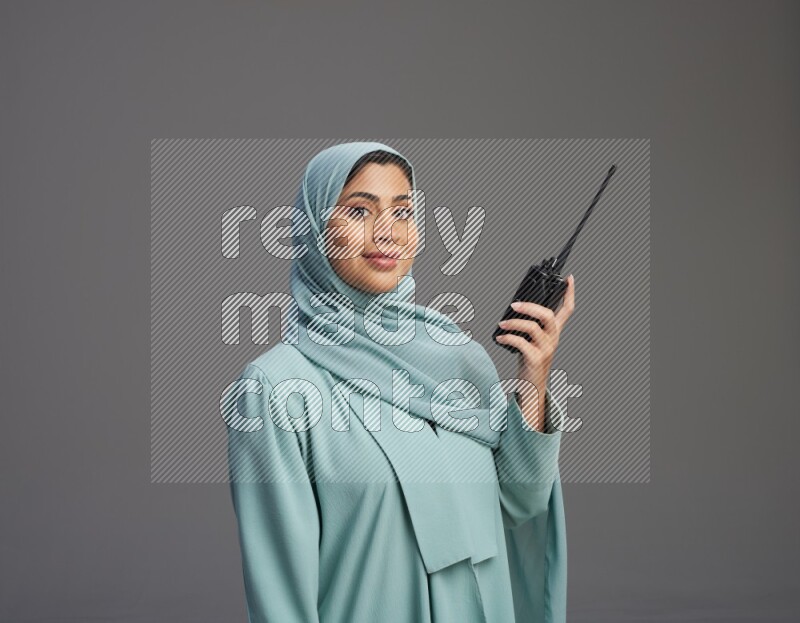 Saudi Woman wearing Abaya standing holding walkie-talkie on Gray background