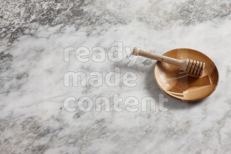 Multicolored pottery plate with wooden honey dipper in it on grey marble background