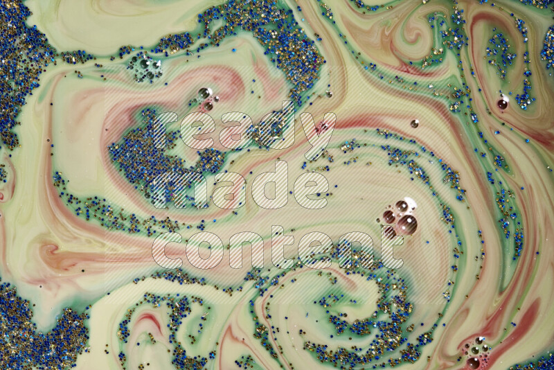 A close-up of sparkling blue and gold glitter scattered on swirling green and red background