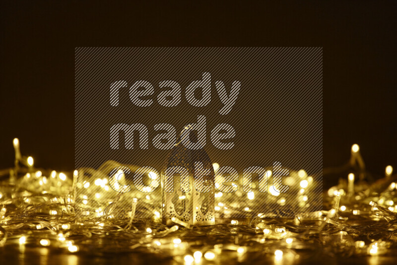 A traditional ramadan lantern surrounded by glowing fairy lights in a dark setup