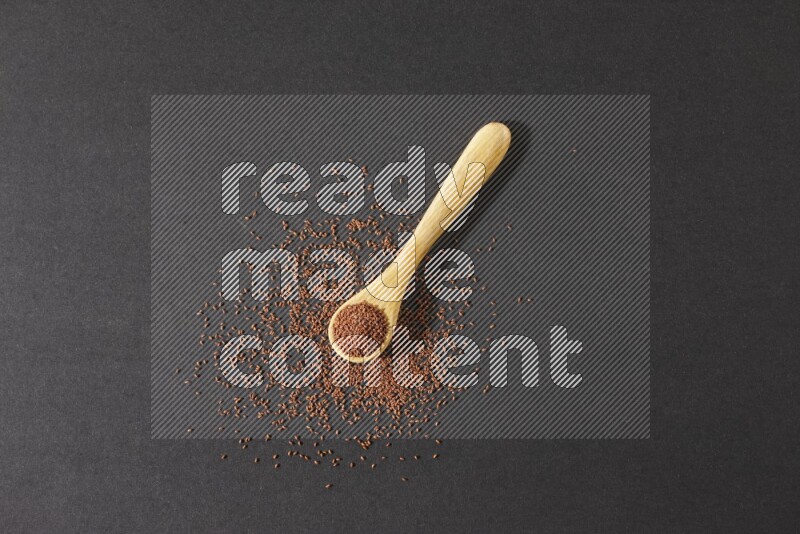 A wooden spoon full of garden cress seeds and seeds spread beside it on a black flooring