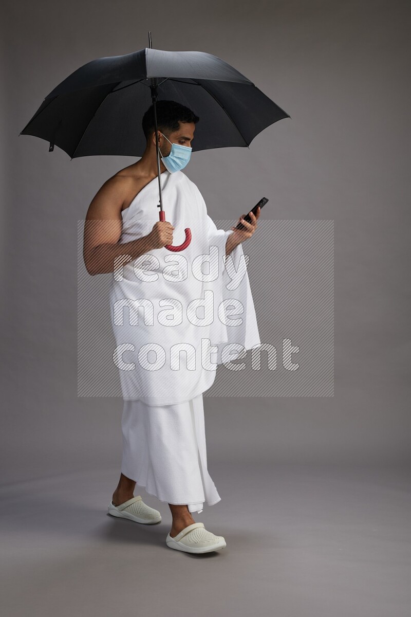 A man wearing Ehram and mask Standing holding umbrella on gray background on gray background