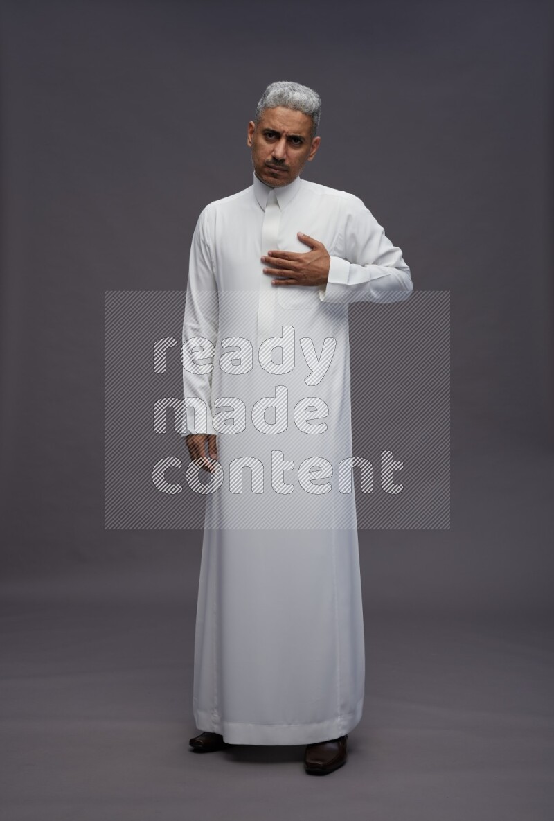 Saudi man wearing thob standing interacting with the camera on gray background