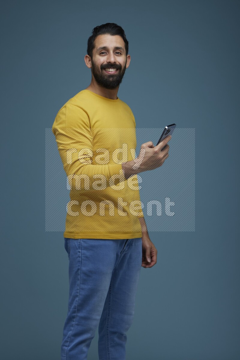 Man posing with a phone in a blue background wearing a yellow shirt