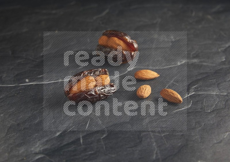 two almond stuffed madjoul dates on a black textured background