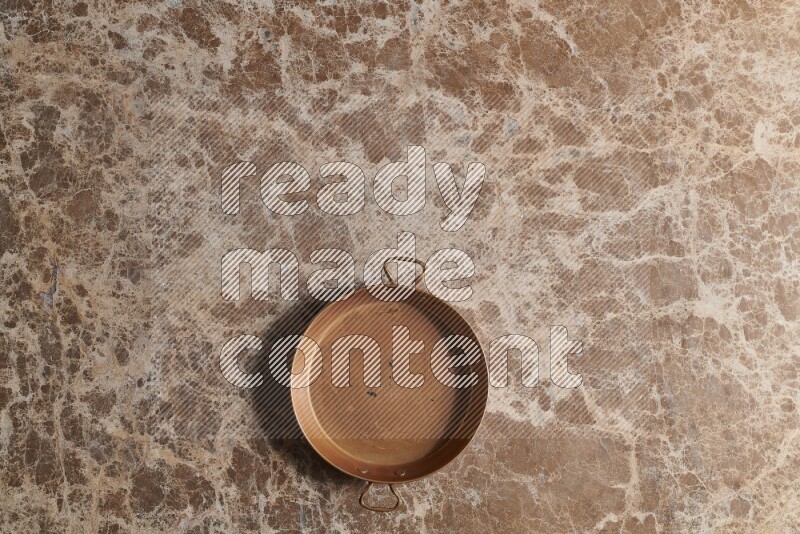 A small copper pan on beige marble background