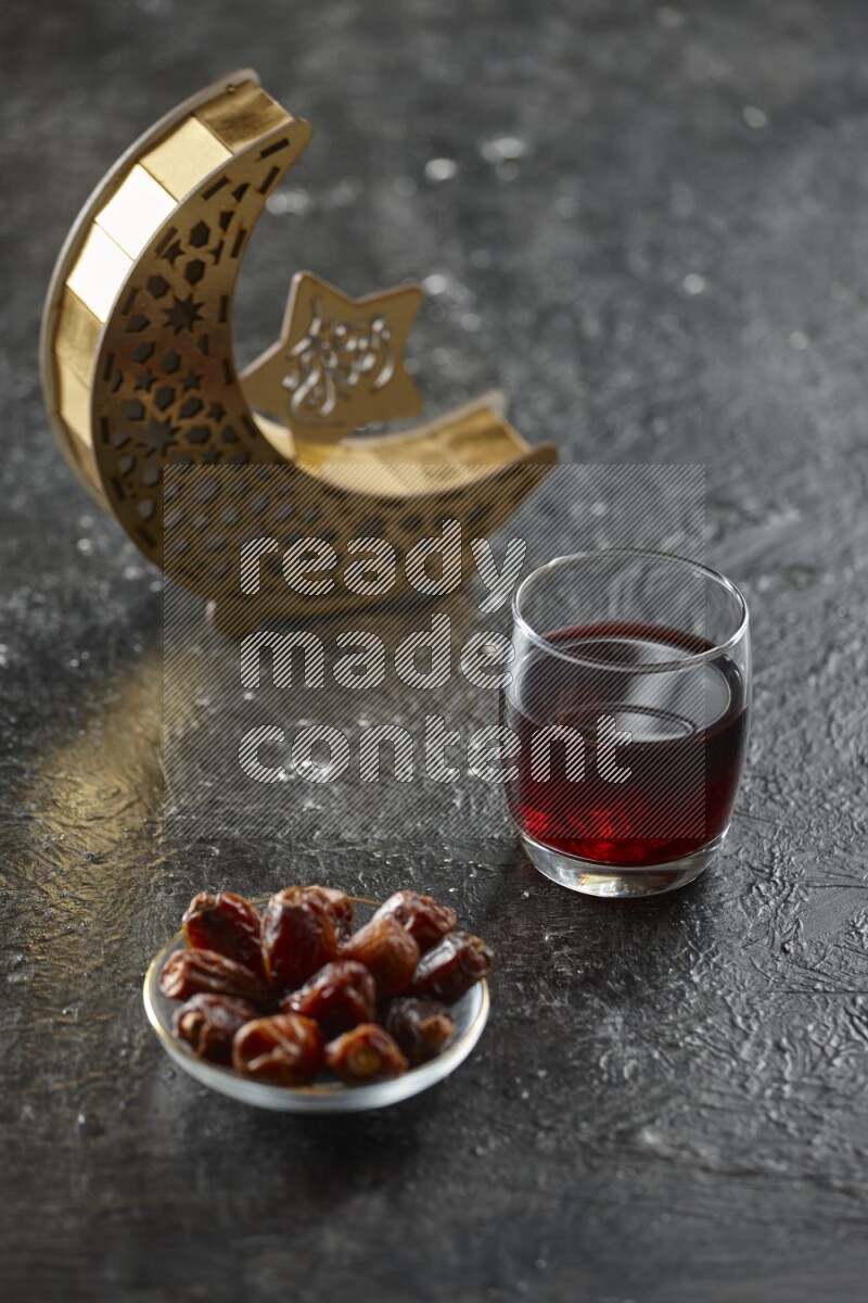 A wooden golden crescent lantern with different drinks, dates, nuts, prayer beads and quran on textured black background