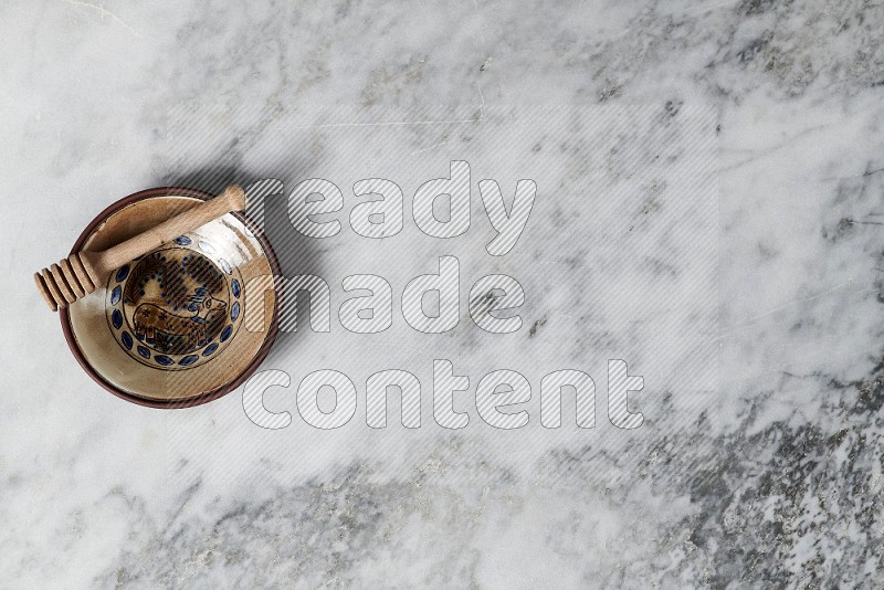 Decorative Pottery Plate with wooden honey handle in it, on grey marble flooring, Top View