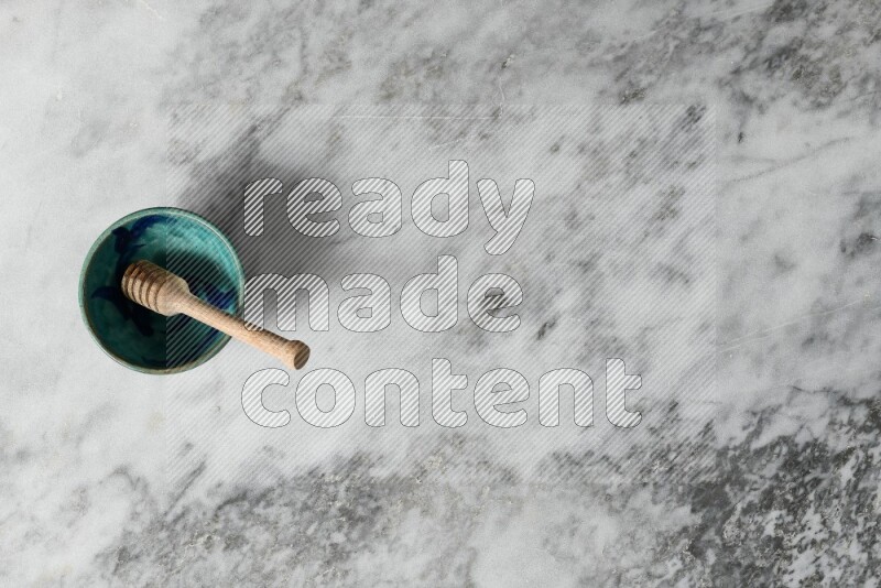 Decorative pottery bowl with wooden honey dipper in it on grey marble background