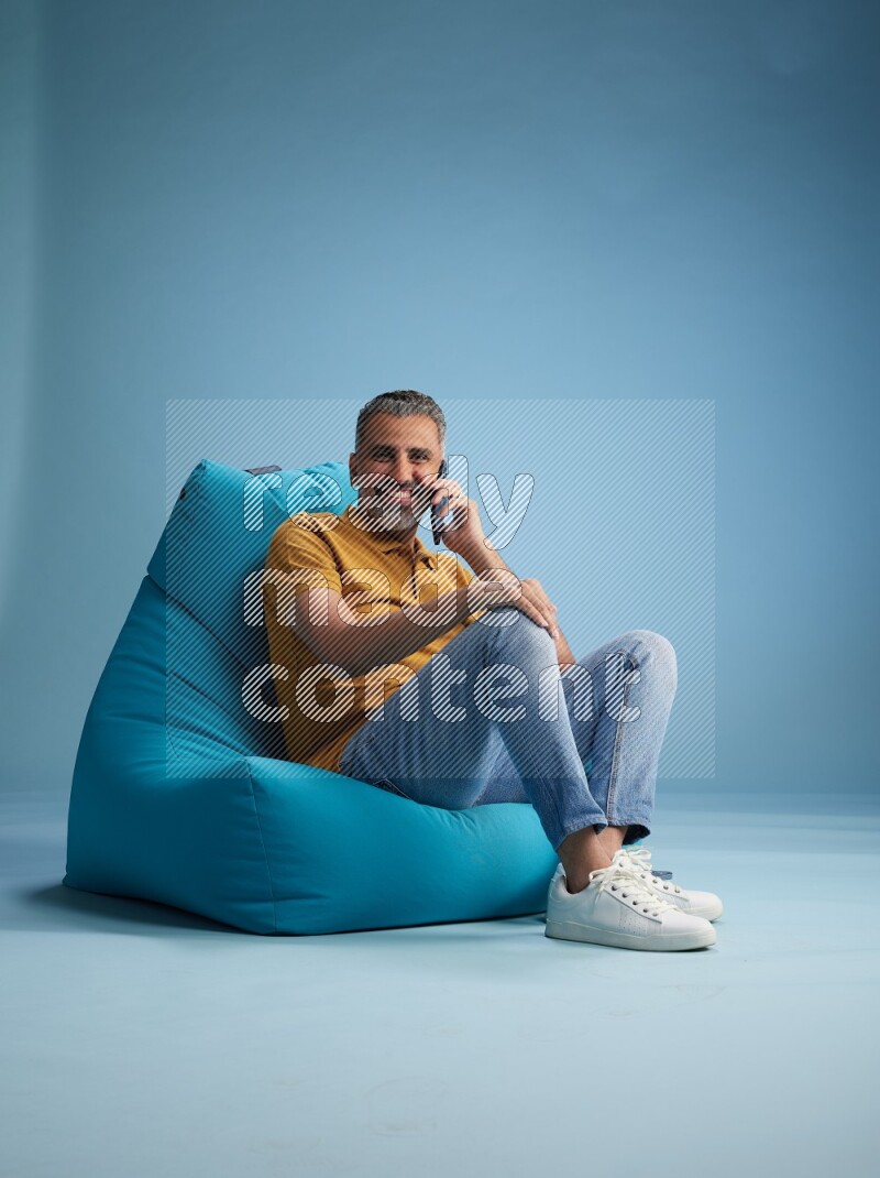 A man sitting on a blue beanbag and talking on the phone