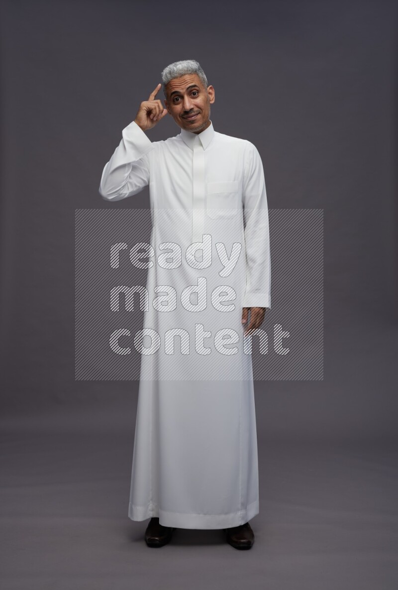 Saudi man wearing thob standing interacting with the camera on gray background