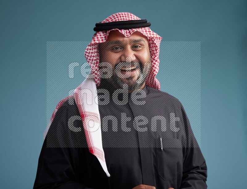 Saudi Man with shimag Standing Interacting with the camera on blue background