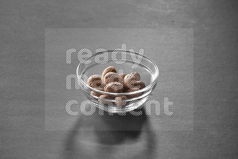A glass bowl full of nutmeg on black flooring