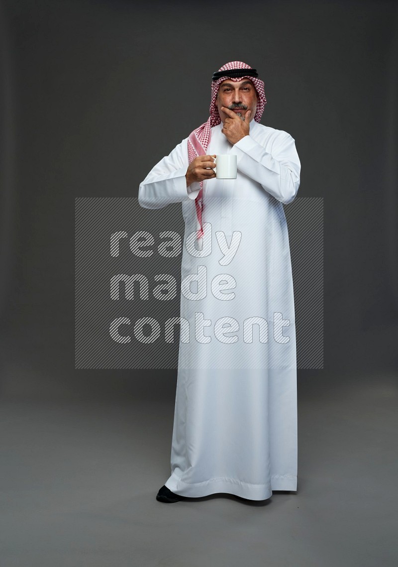 Saudi man with shomag Standing holding mug on gray background