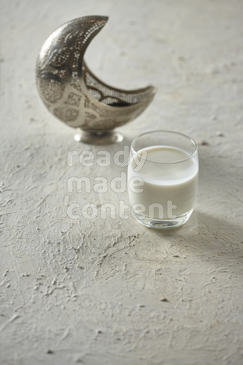 A silver lantern with different drinks, dates, nuts, prayer beads and quran on textured white background