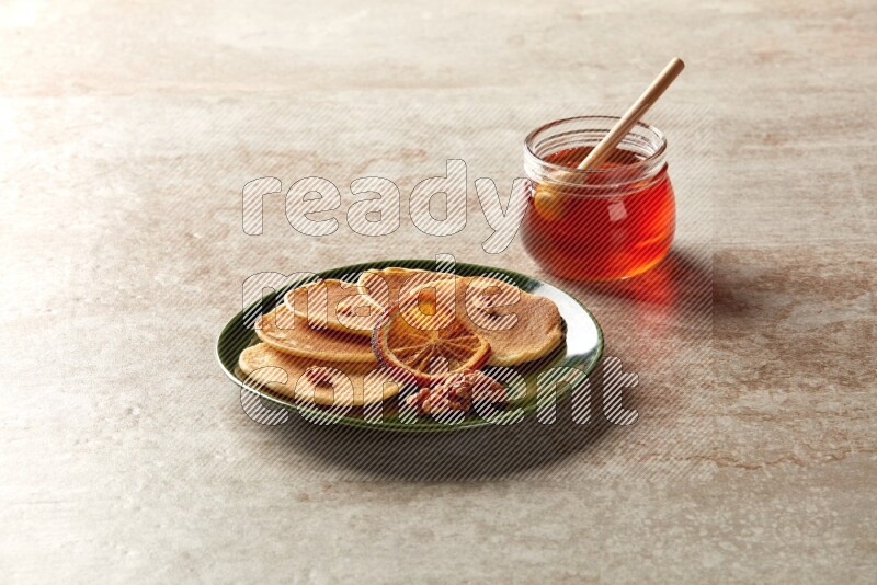 Five stacked dried orange mini pancakes in a green plate on beige background