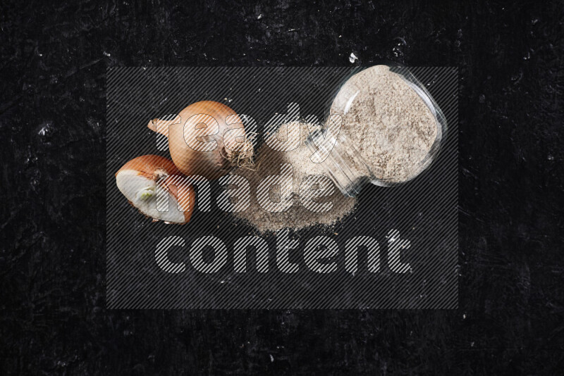 A glass jar full of onion powder flipped with some spilling powder on black background