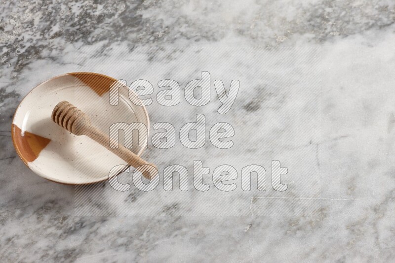 Multicolored pottery plate with wooden honey dipper in it on grey marble background