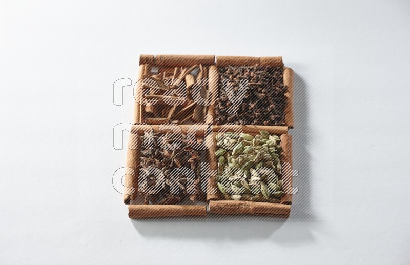 4 مربعات من أعواد القرفة ممتلئة بالهيل واليانسون النجمي والقرنفل والقرفة على أرضية بيضاء