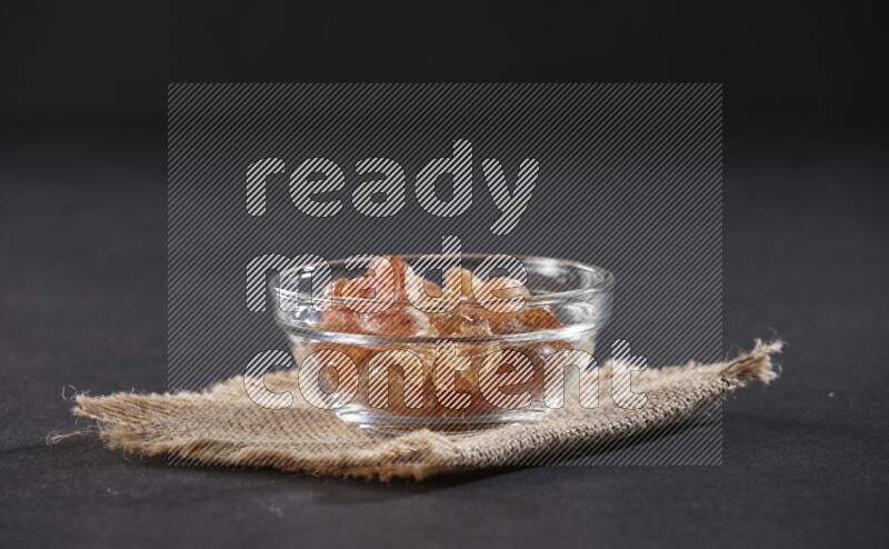 A glass bowl full of gum arabic on a burlap piece on black flooring