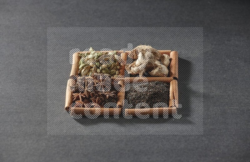 4 مربعات من عيدان القرفة ممتلئة بالشاي واليانسون النجمي والزنجبيل المجفف وحب الهيل على أرضية سوداء