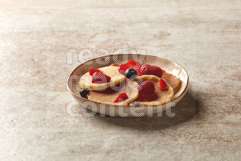 Five stacked mixed berries mini pancakes in an irregular plate on beige background