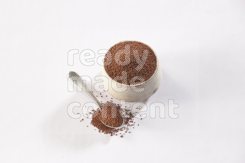 A beige pottery bowl and a metal spoon full of garden cress seeds on a white flooring