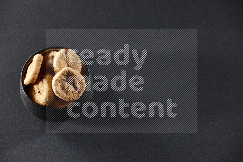 وعاء فخاري أسود ممتلئ بالتين المجفف على خلفية سوداء