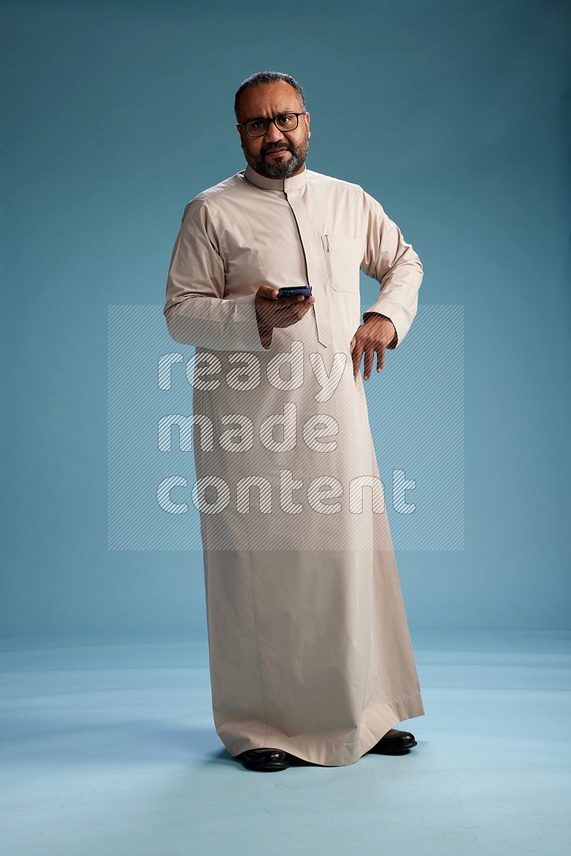 Saudi Man without shimag Standing texting on phone on blue background