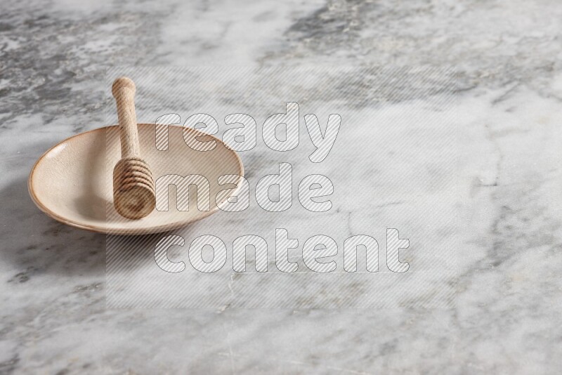 Beige pottery plate with wooden honey dipper in it on grey marble background