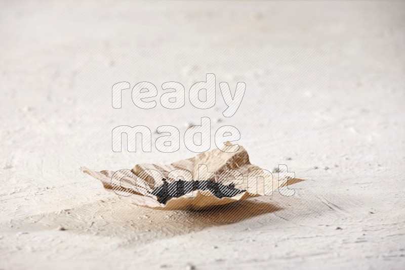 A crumpled piece of paper full of black seeds on a textured white flooring in different angles