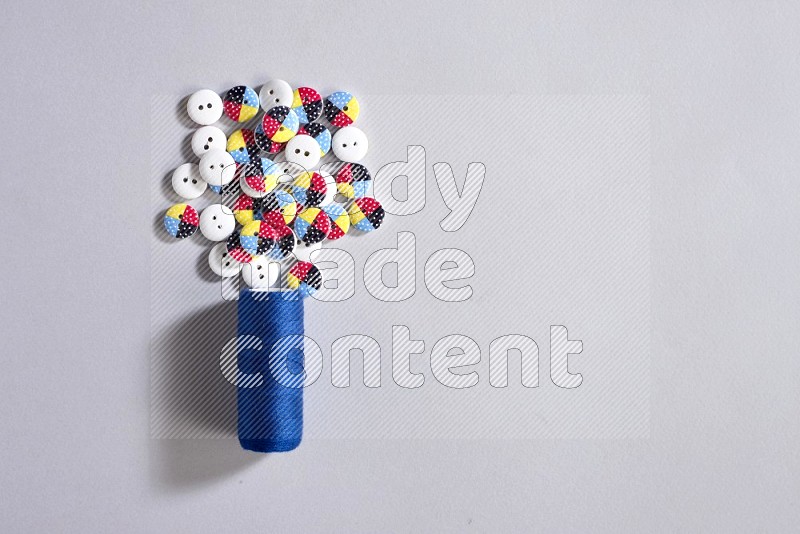 A blue sewing thread spool with colored buttons on grey background