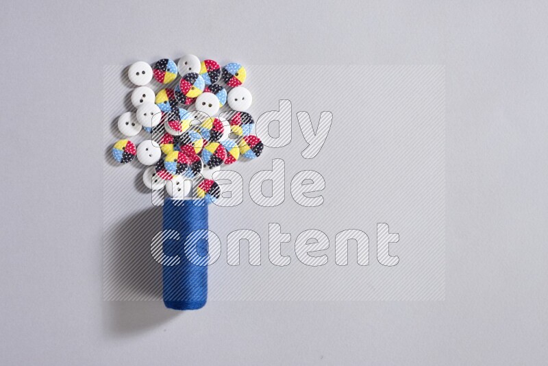A blue sewing thread spool with colored buttons on grey background