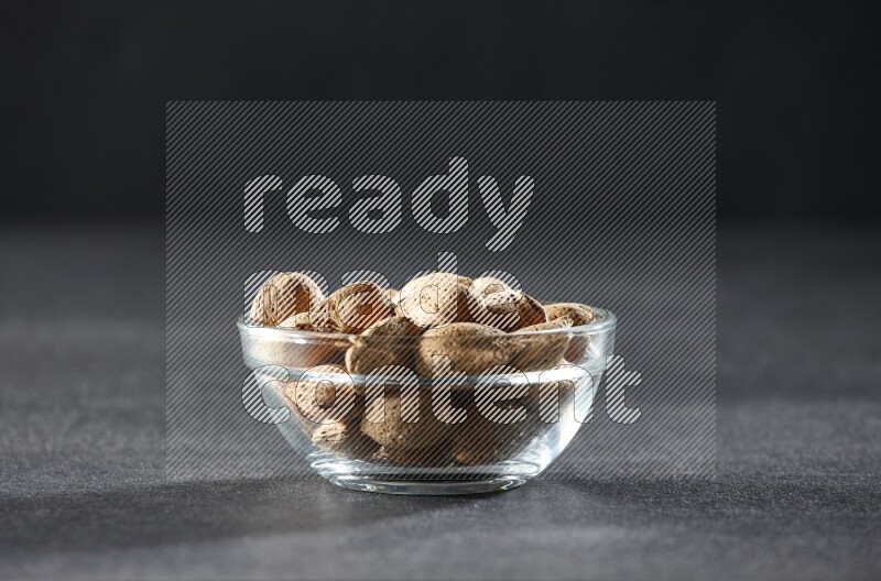 A glass bowl full of almonds on a black background in different angles